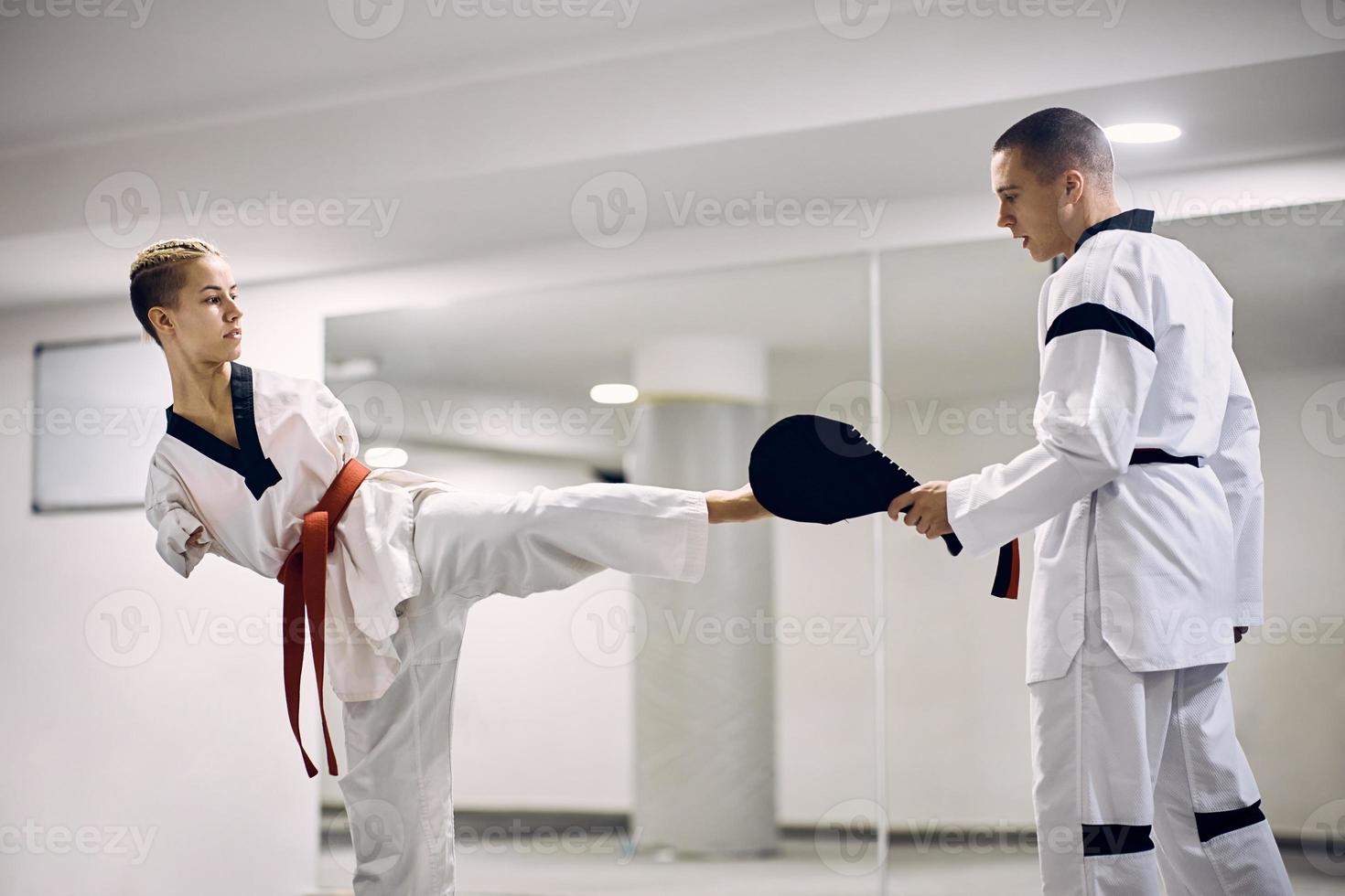 gemotiveerd atletisch vrouw met een onbekwaamheid beoefenen been trap met taekwondo trainer in Gezondheid club. foto