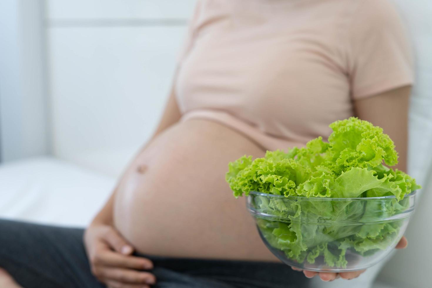 een zwanger vrouw houdt een kop van groen groenten. aan het eten gezond voedsel voor de ongeboren kind foto