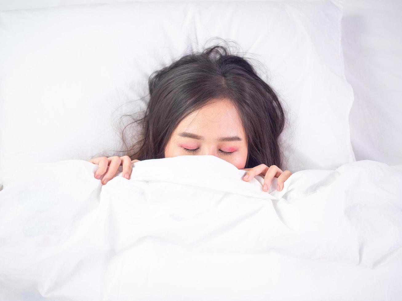 jong vrouw slapen sliep terwijl aan het liegen in bed comfortabel en gelukkig. beide handen getrokken omhoog de deken bijna aan het bedekken de gezicht. foto