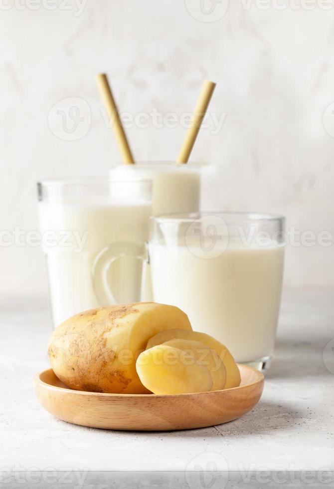 veganistisch aardappel melk in bril, besnoeiing aardappel knol Aan houten bord Aan licht neutrale achtergrond. foto