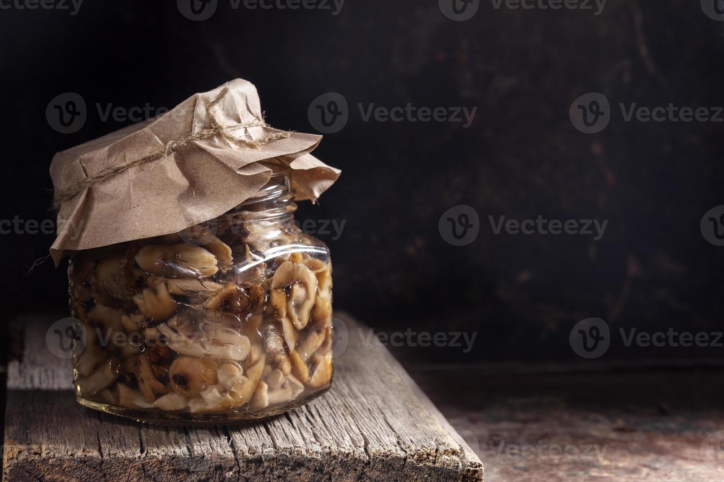 glas pot met gepekeld champignons honing zwammen onder papier Hoes Aan oud houten bord Aan donker roestig metaal achtergrond. foto