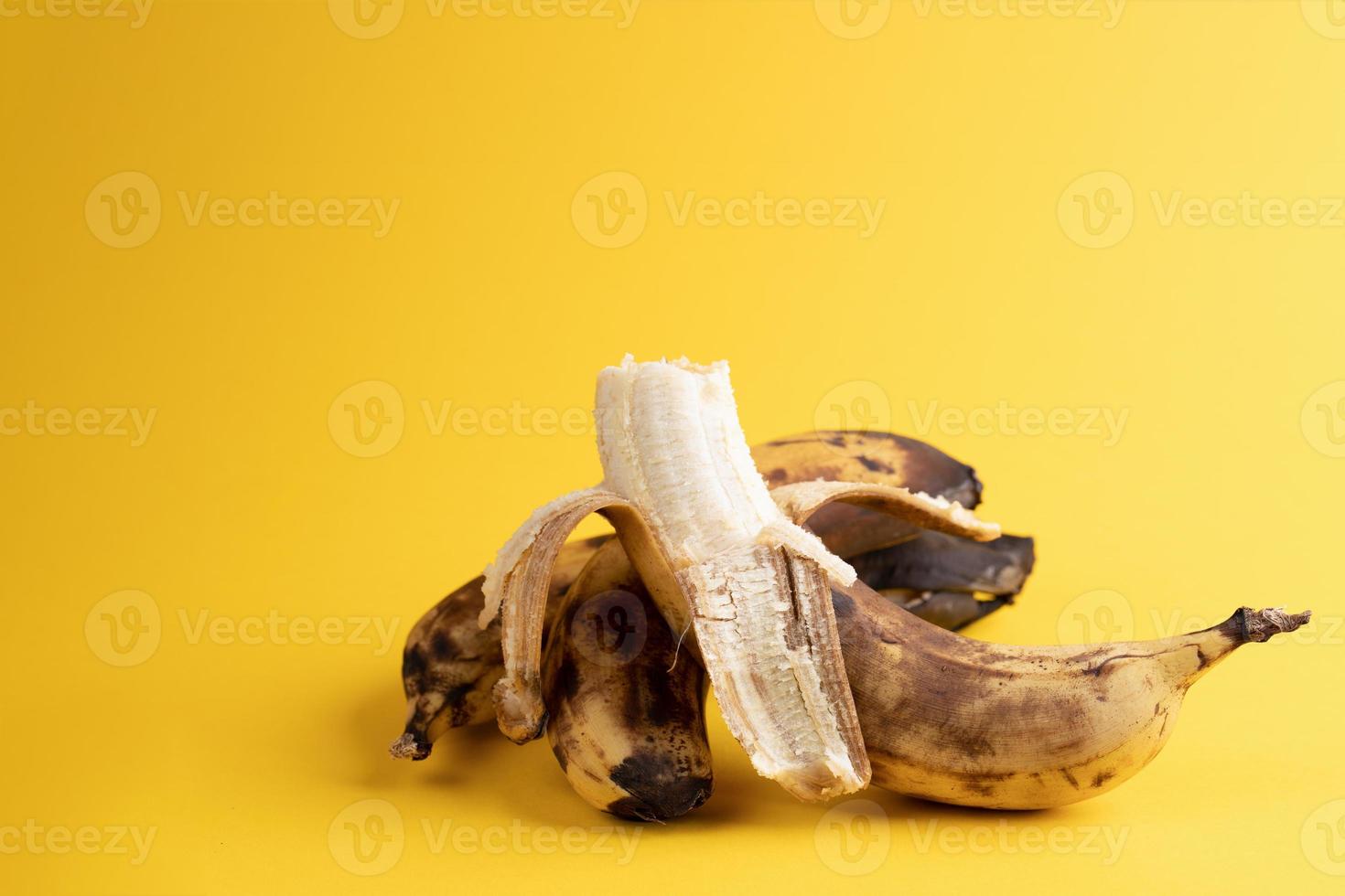 een geschild banaan en twee ongeschild overrijp zwart gemaakt lelijk bananen Aan helder geel achtergrond. foto