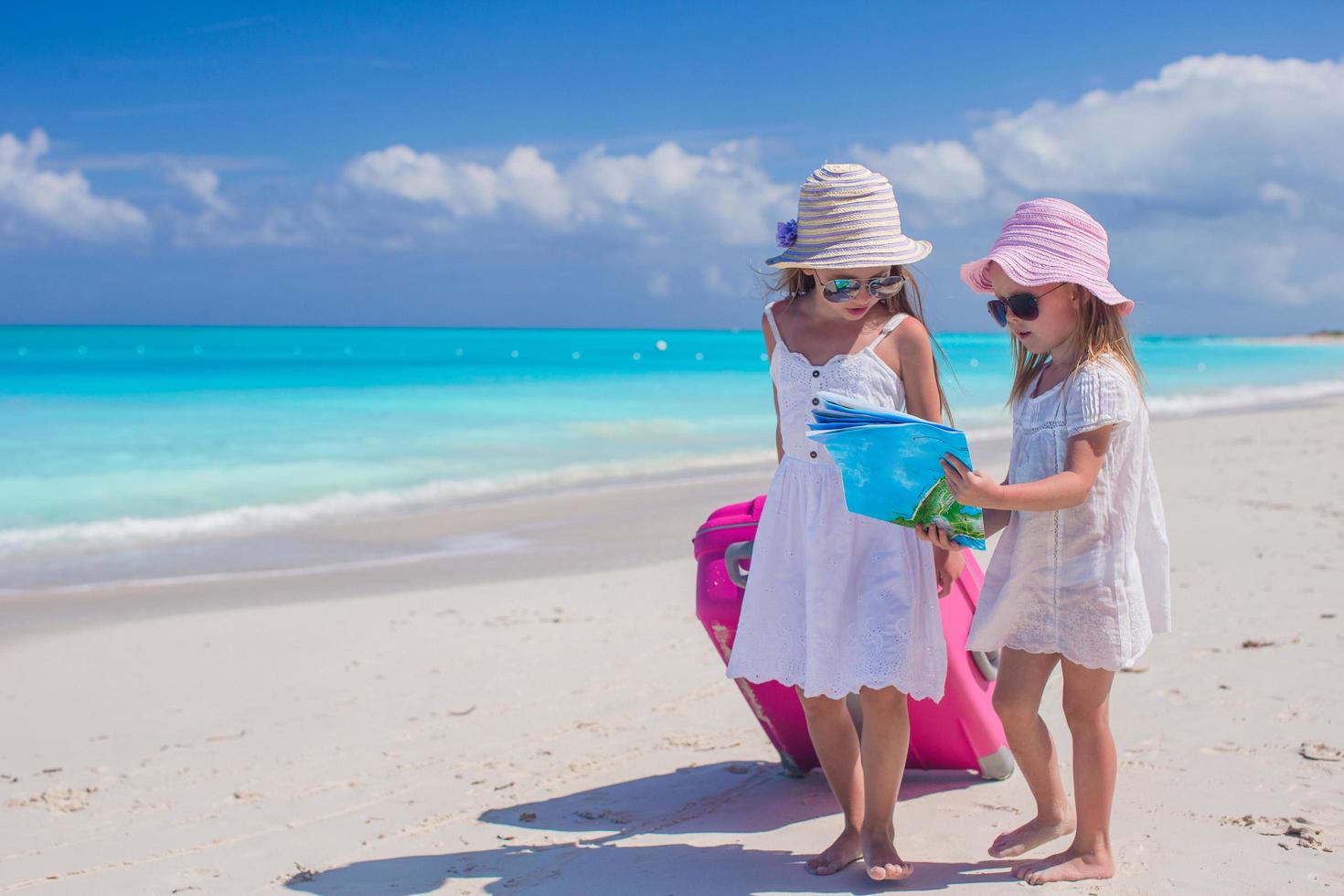 meisjes lopen met een koffer en een kaart op een strand foto