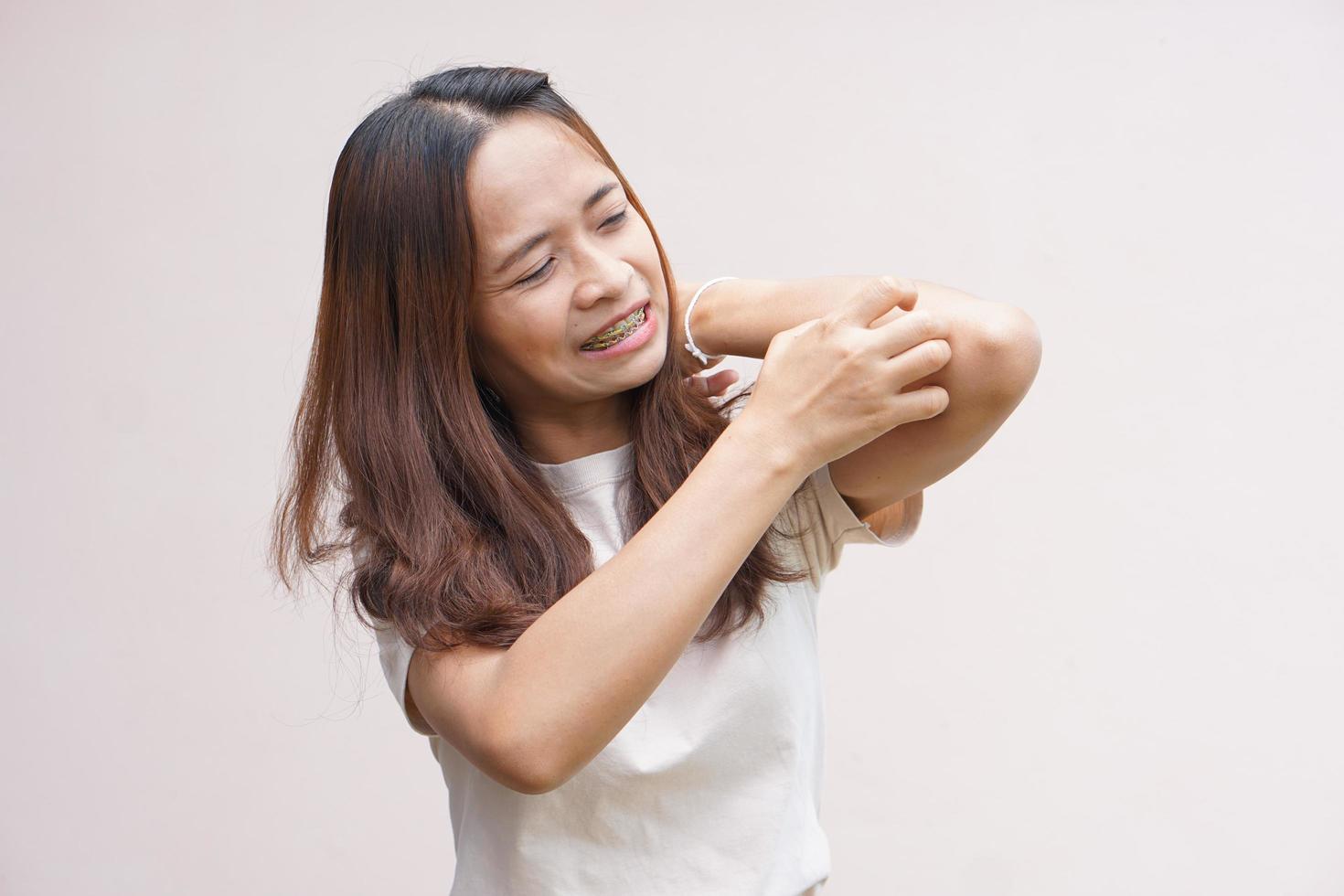 vrouw krabben arm van jeuk op lichtgrijze achtergrond. oorzaak van jeukende huid omvatten insectenbetenconcept van gezondheidszorg huid foto