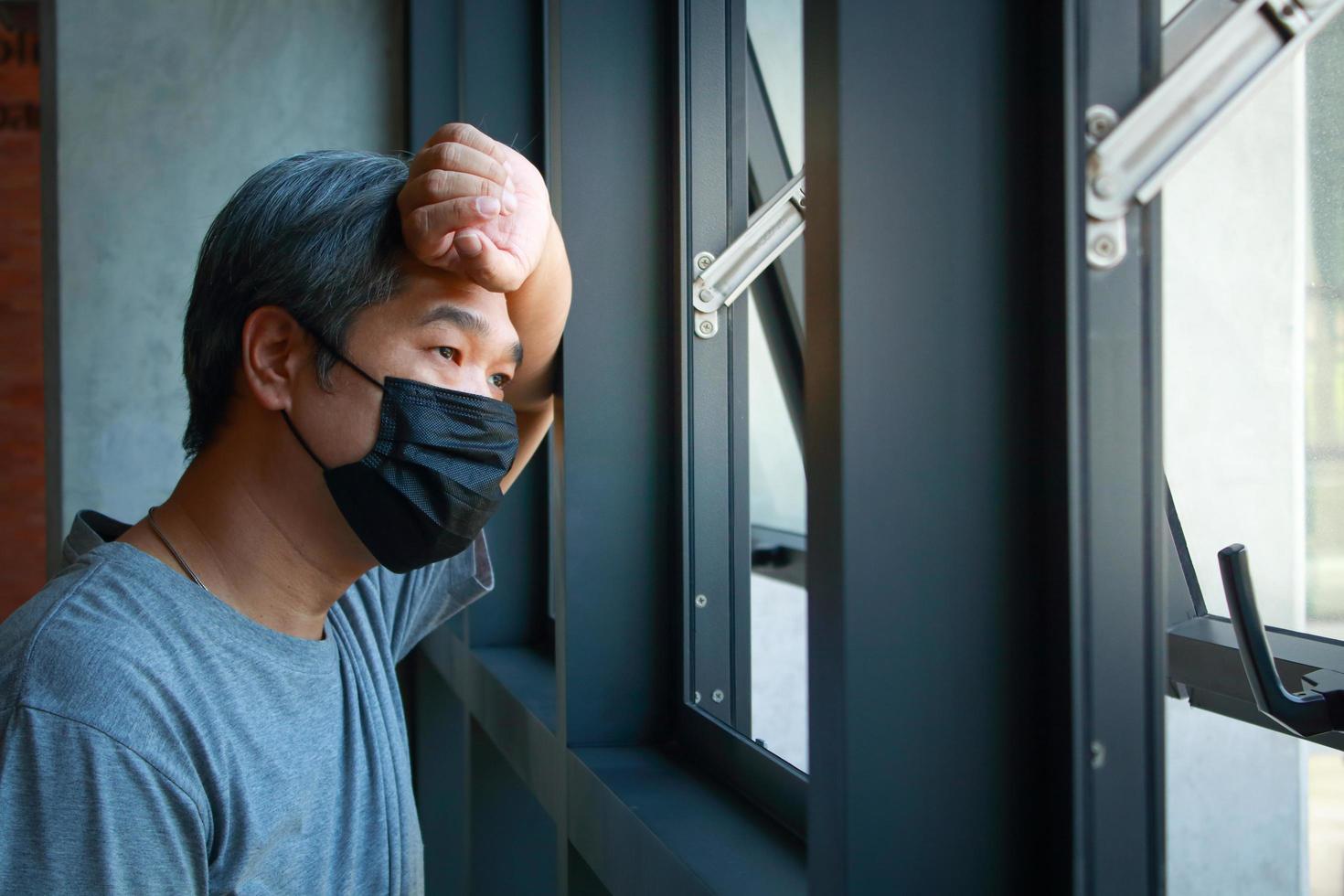 benadrukt Aziatisch ouderen Mens slijtage een zwart masker hand- Holding de voorhoofd op zoek buiten de venster. concept van Gezondheid problemen voor de ouderen, leven bedenkingen gedurende de verspreiding van coronavirus ziekte. foto