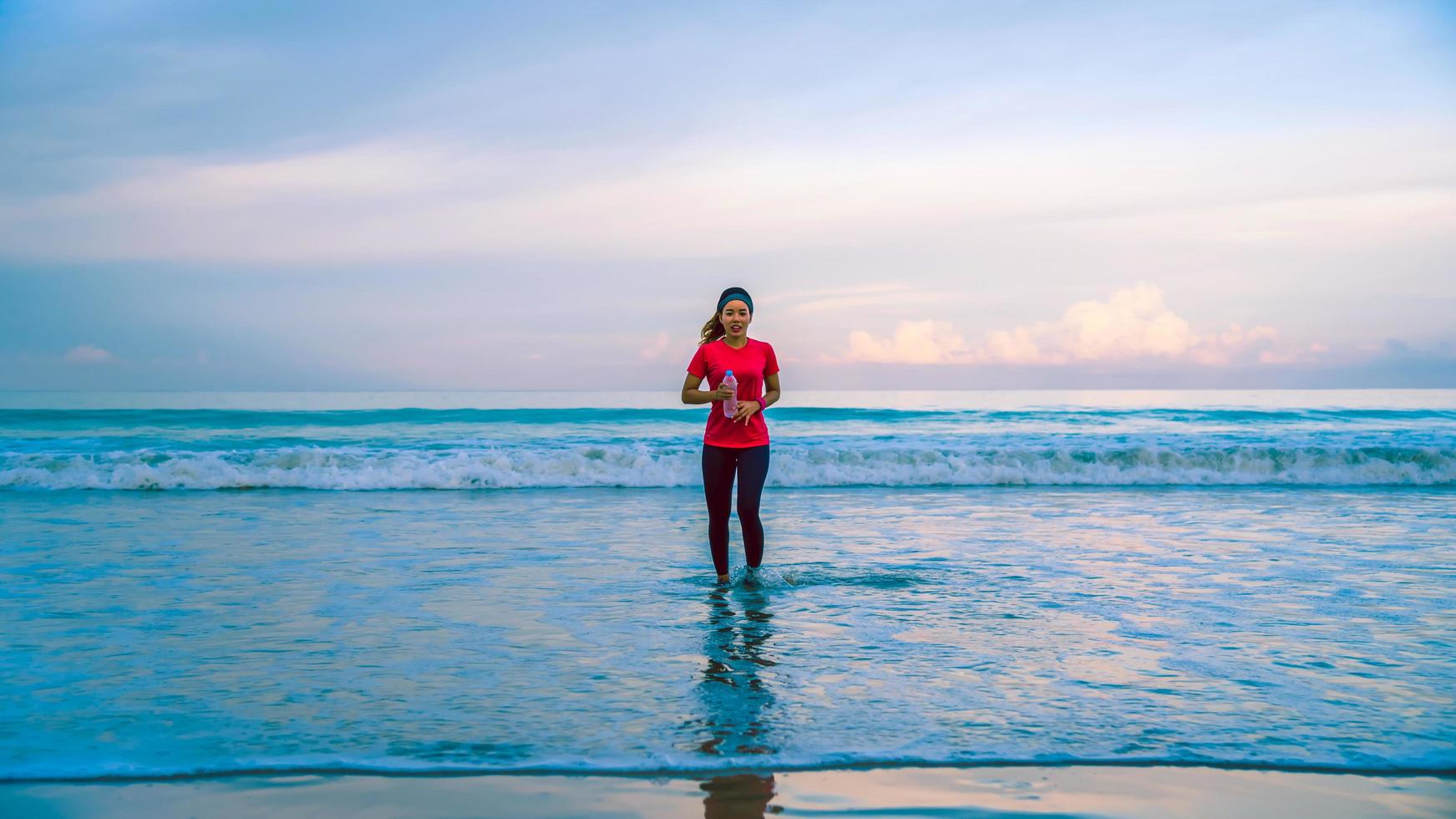 meisje met training joggen op het strand in de ochtend. ontspannen en blij zijn met hardlopen op zee. in de zomer foto