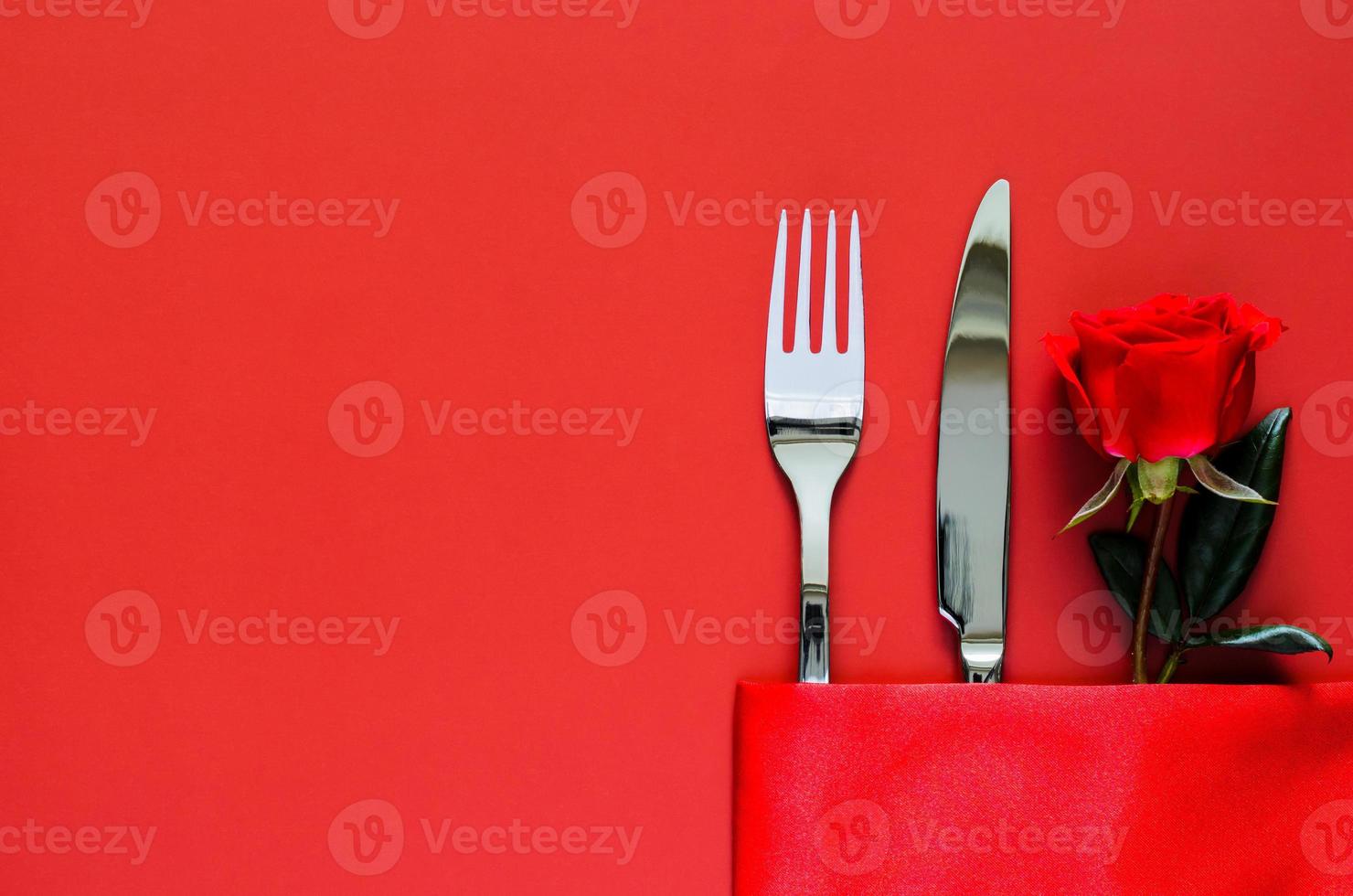 vork en mes met rood roos zetten in servet Aan rood tafel voor valentijnsdag dining concept. foto