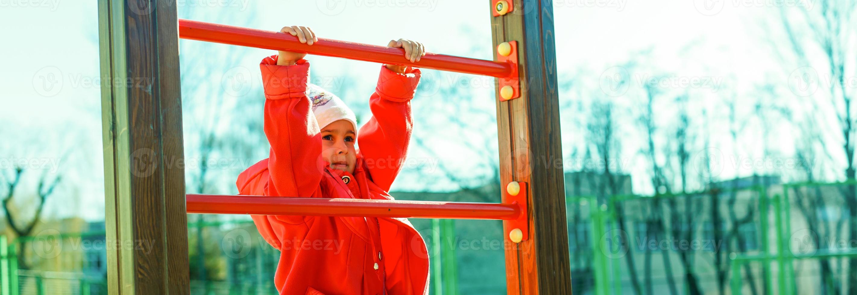 portret van gelukkig weinig meisje spelen Aan een touw web speelplaats buitenshuis foto