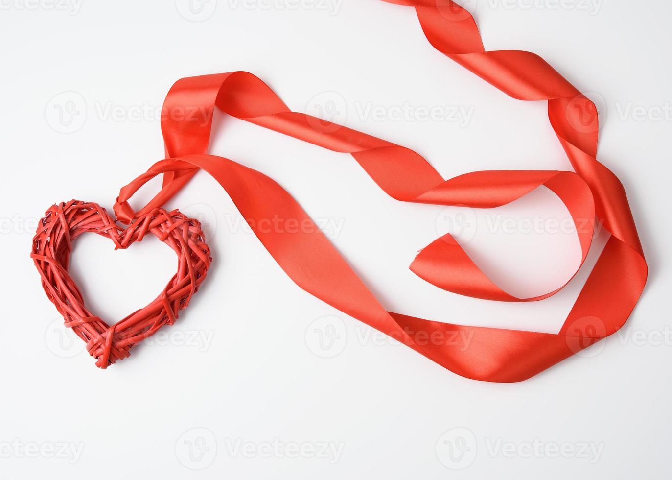 rood gevlochten hart en gedraaid zijde lint Aan wit achtergrond foto