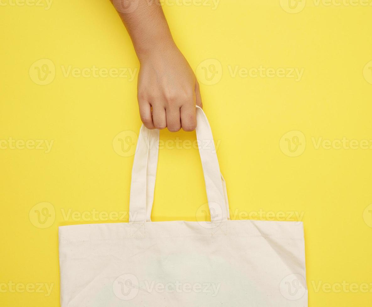 vrouw hand- houdt een leeg beige textiel zak door de handvatten Aan een geel achtergrond foto