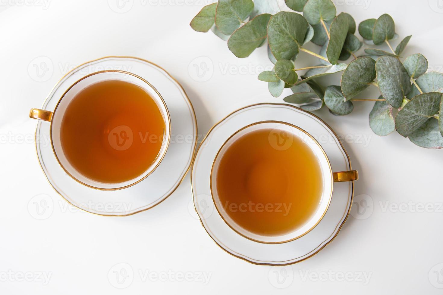 twee cups van thee zijn Aan de tafel, een Afdeling van eucalyptus. zwart thee in een porselein mooi wit kop met een gouden snee. foto