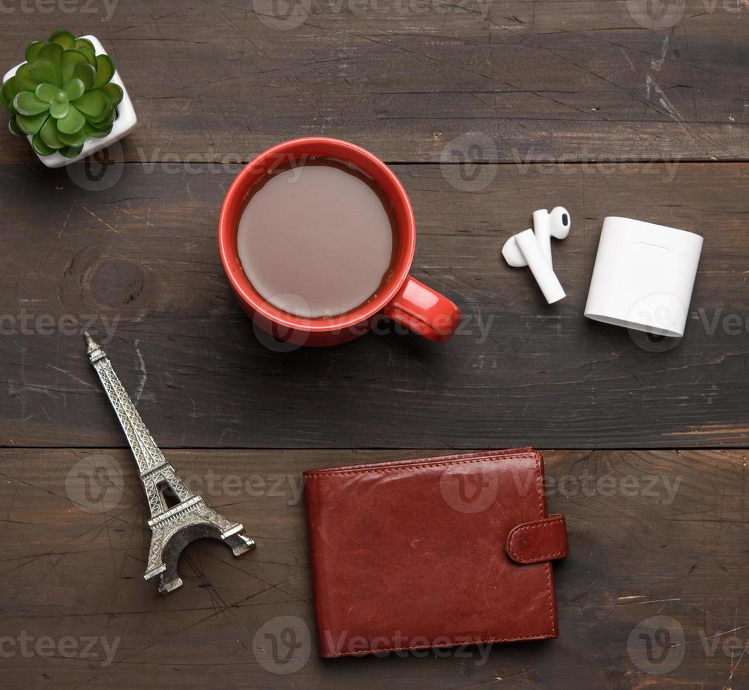 rood keramisch mok met zwart koffie, leer bruin portemonnee en draadloze hoofdtelefoons foto