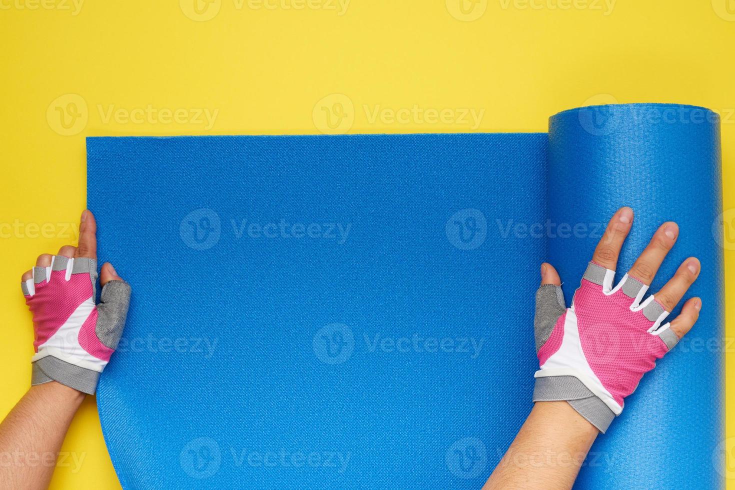 twee vrouw handen in sport- handschoenen ontvouwen een blauw yoga mat foto