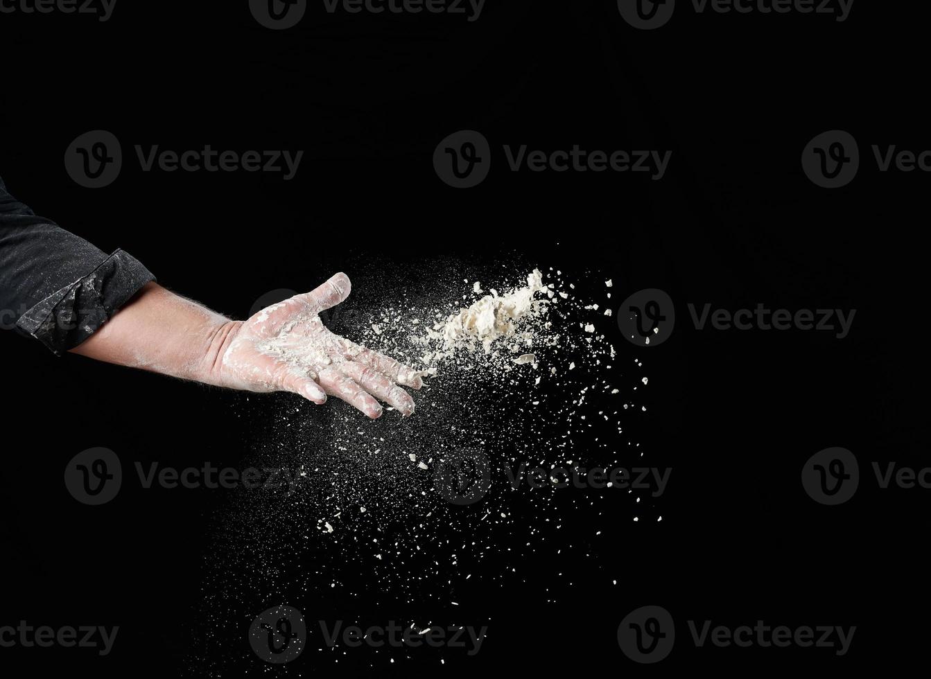 bakker mannetje hand- gooit omhoog een handvol van wit tarwe meel Aan een zwart achtergrond foto