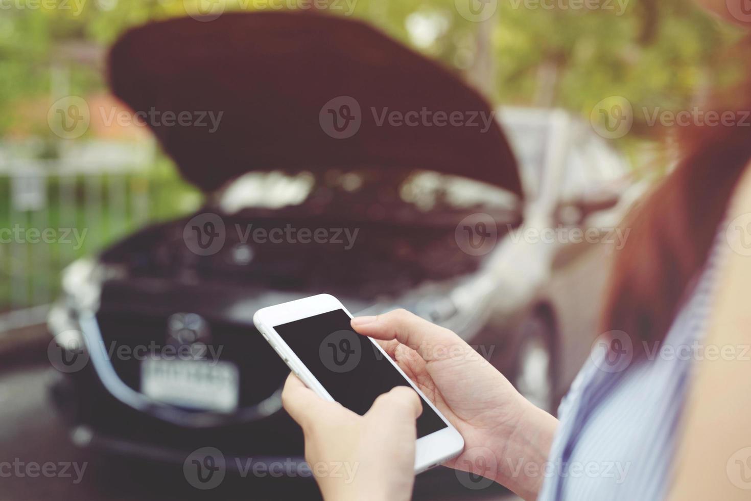 close-up vrouwelijke hand met behulp van een mobiele smartphone oproep een automonteur om hulp vragen omdat de auto kapot is langs de weg. leeg of leeg scherm. foto