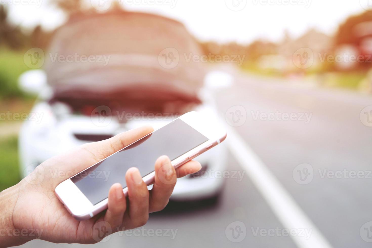 close-up vrouwelijke hand met behulp van een mobiele smartphone oproep een automonteur om hulp vragen omdat de auto kapot is langs de weg. leeg of leeg scherm. foto