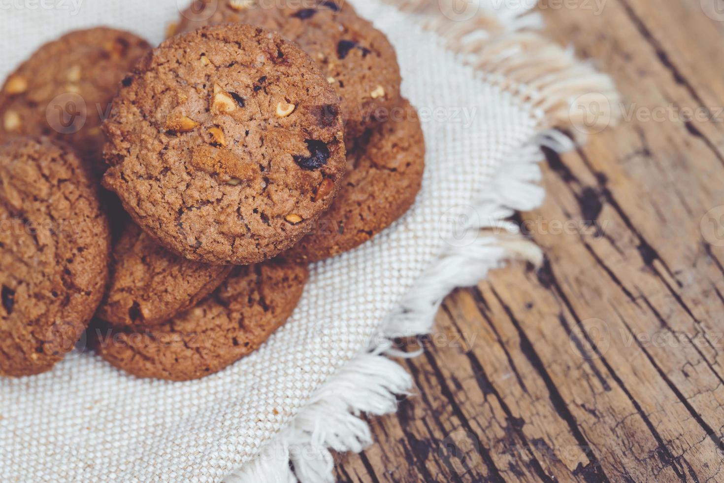 dichtbij omhoog van een groep chocola spaander koekjes veel gestapeld Aan schort zak donker oud rustiek houten plank tafel met vertrekken kopiëren ruimte plaats voor tekst. vers gebakken. toetje foto