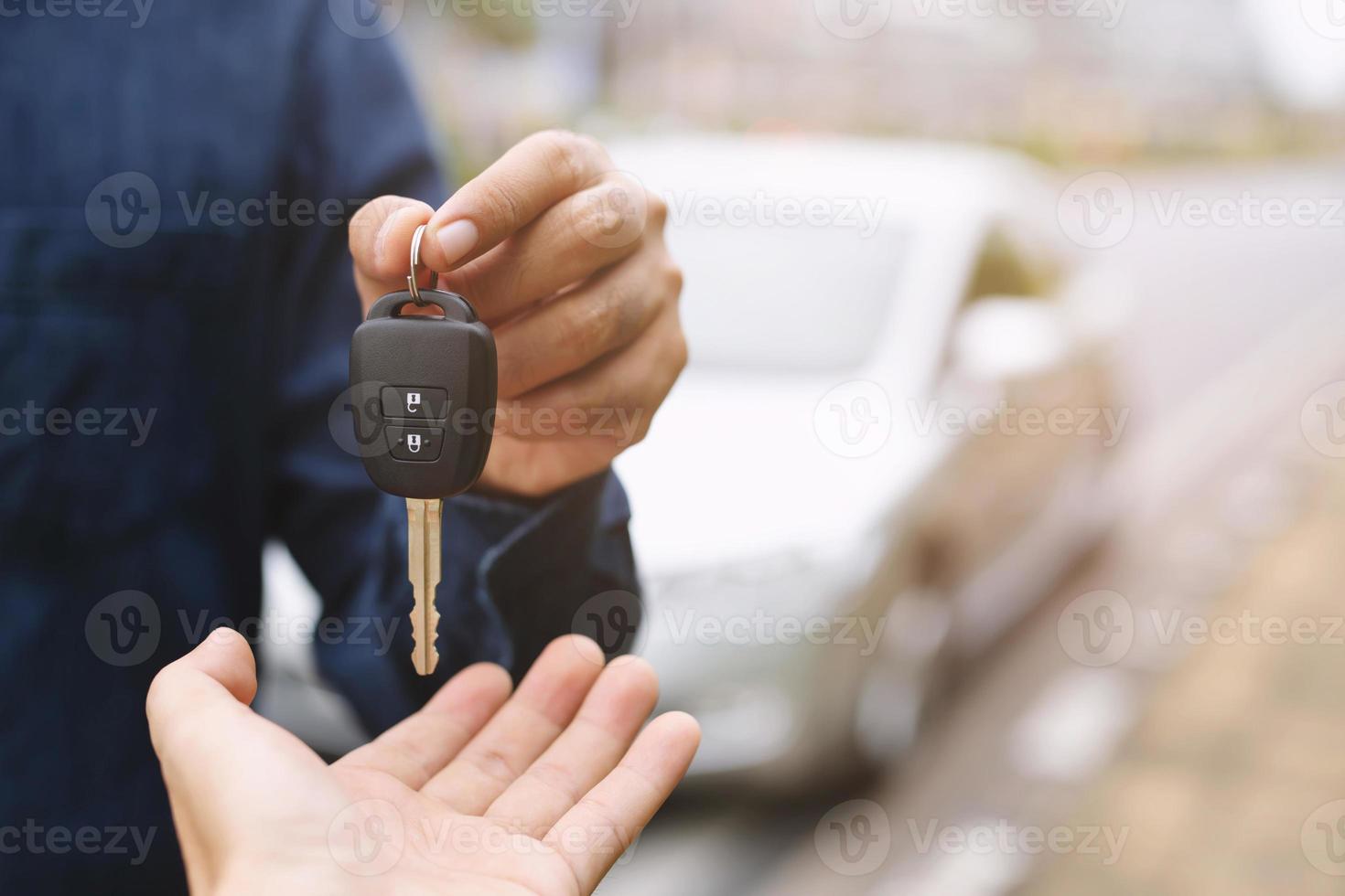 autosleutel, zakenman overhandigen geeft de autosleutel aan de andere vrouw op de achtergrond van de auto. foto