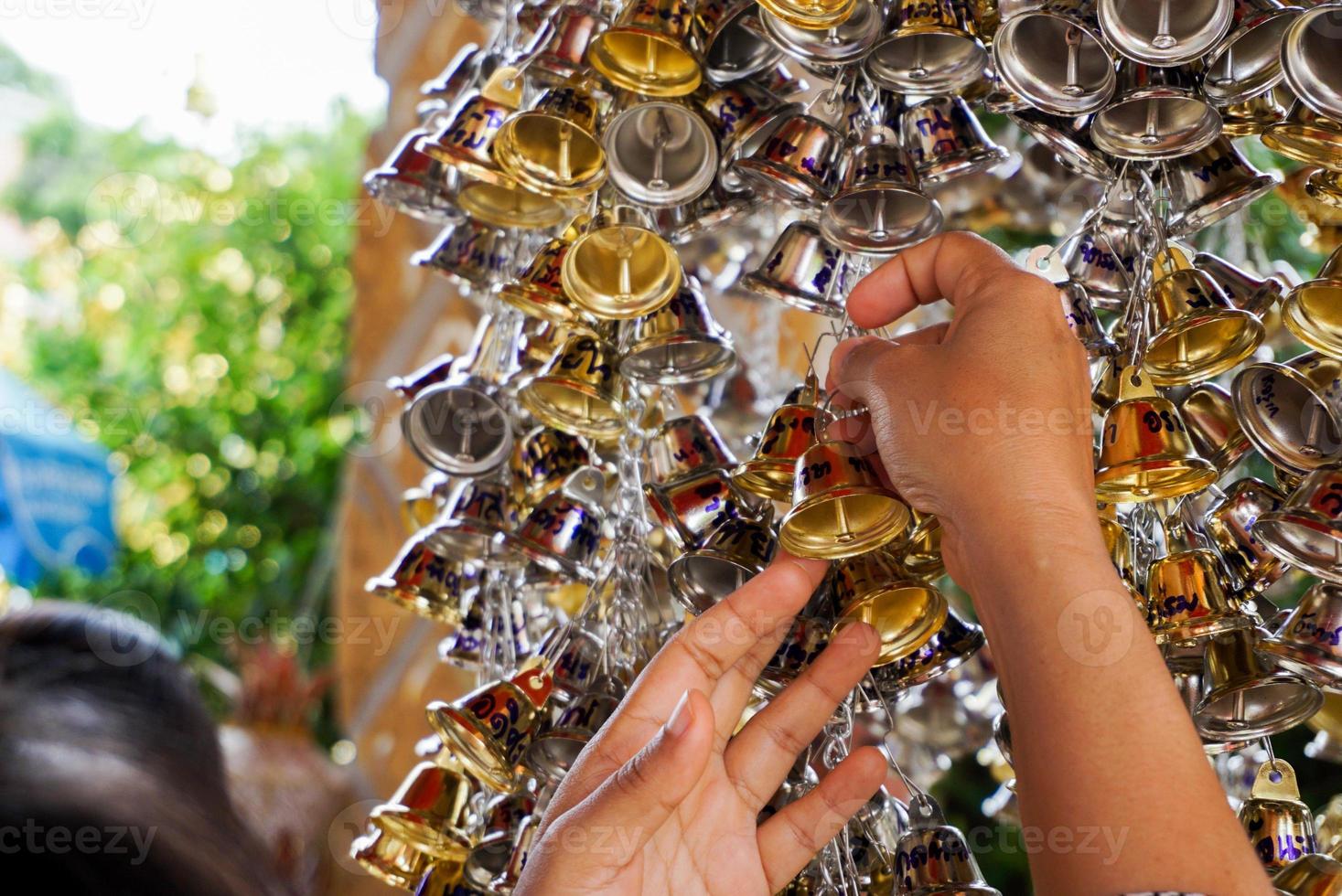 dichtbij omhoog hand- grijp klein gouden en zilver klokken naar hangende in Thais tempel. foto