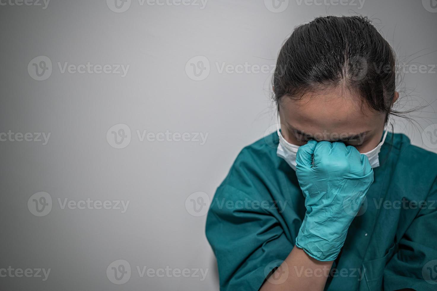 vermoeide depressieve vrouwelijke Aziatische scrubverpleegster draagt gezichtsmasker blauw uniform zit op de ziekenhuisvloer, jonge vrouwelijke arts gestrest van hard werken foto