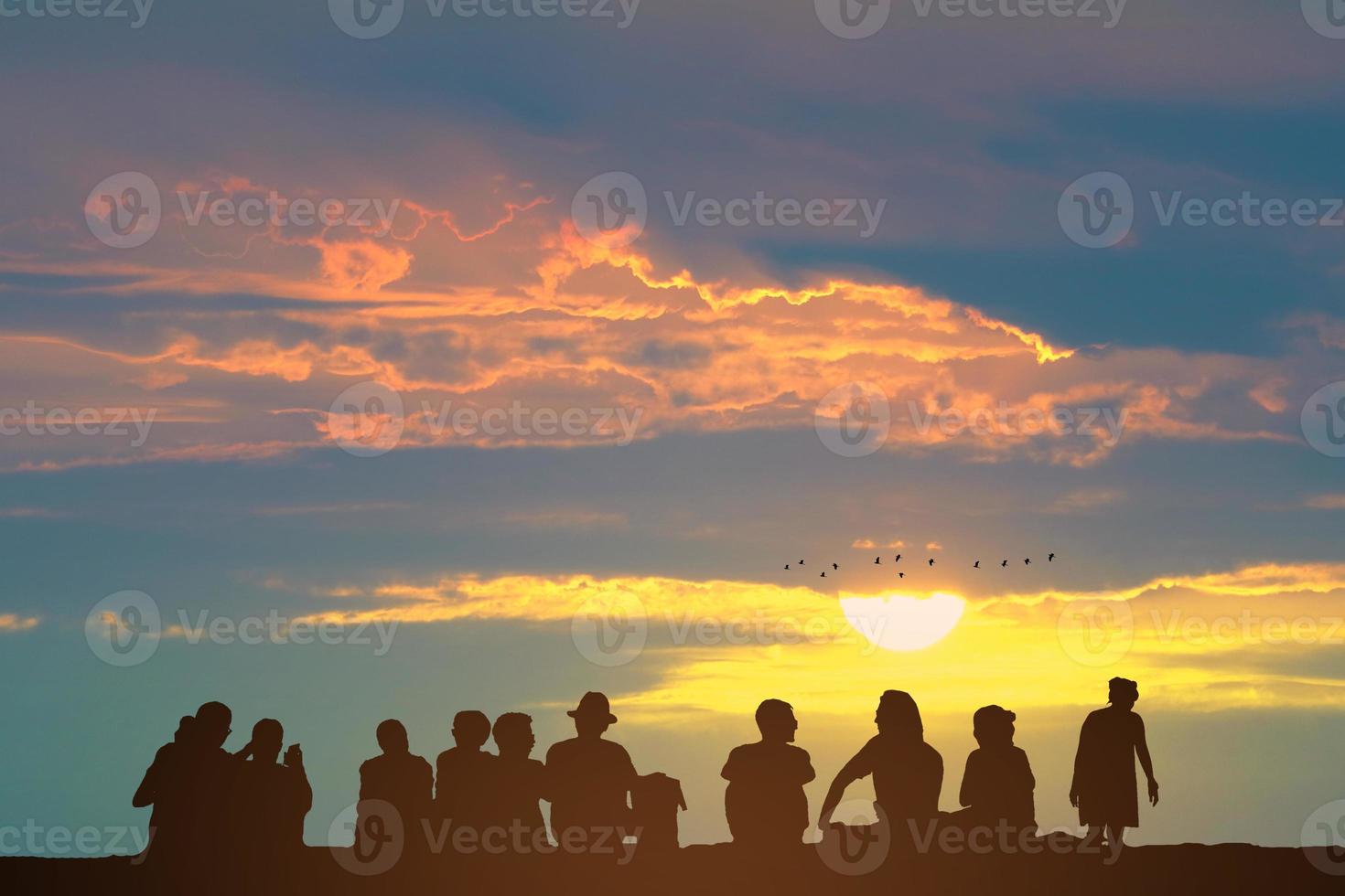 silhouet mensen zittend Aan de verdieping en zonsondergang Aan de kleurrijk lucht oranje wolk en vogelstand vliegend foto