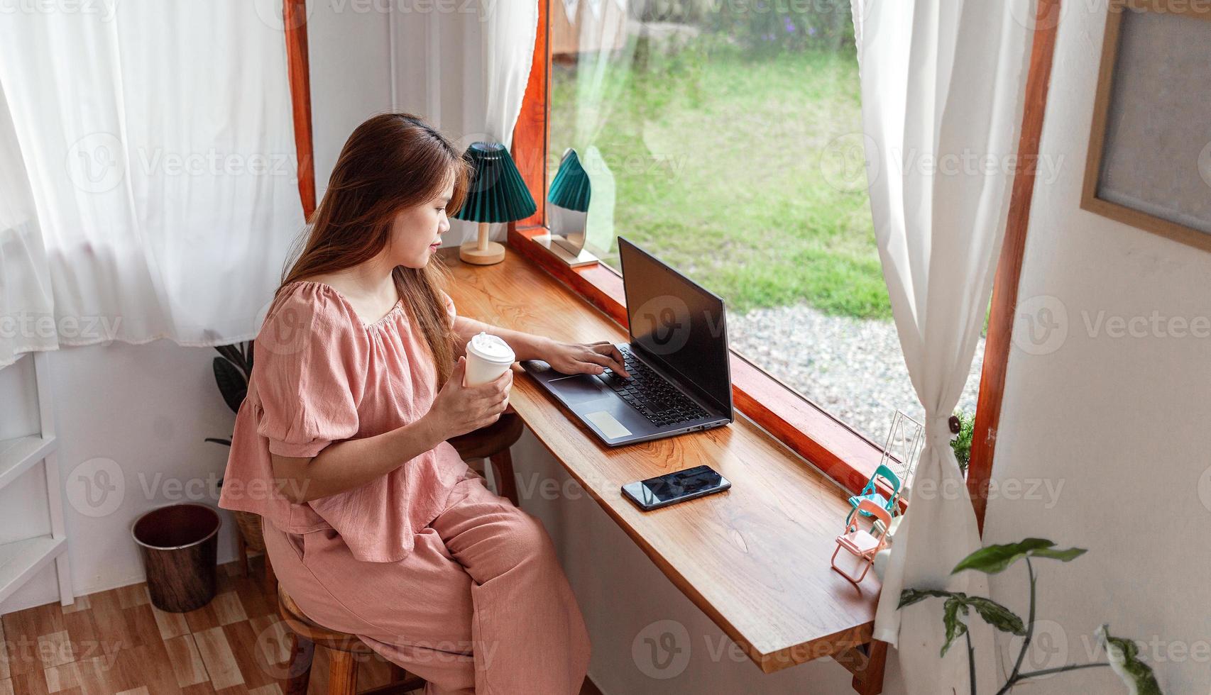 een gelukkig vrouw Bij een cafe gebruik makend van een laptop in hand- en een papier kop van koffie. jong wit vrouw met lang haar- zittend in een koffie winkel bezig werken Aan haar laptop. foto