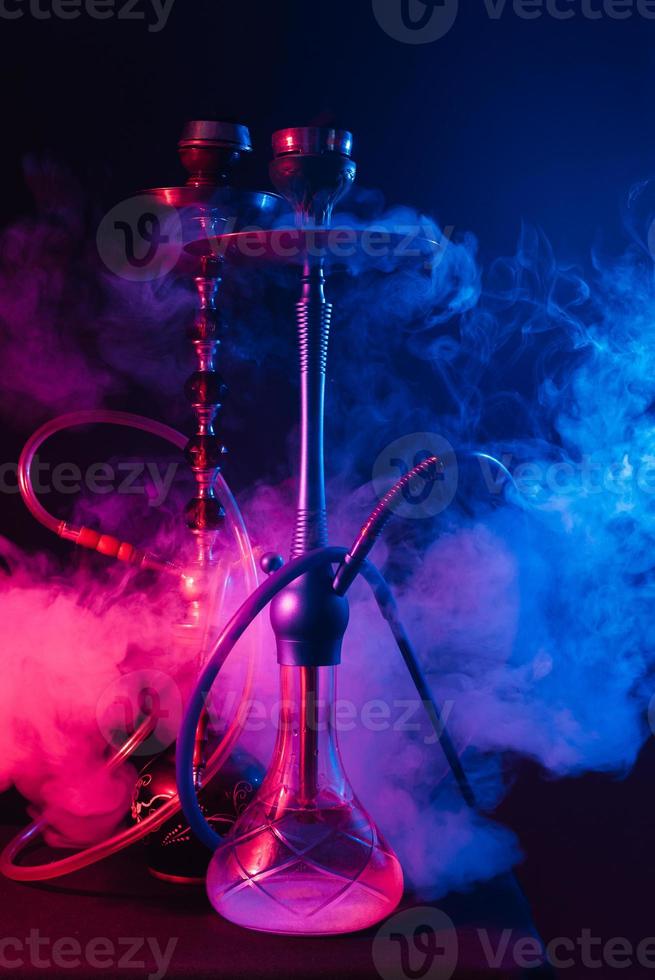 modieus hookah met een wolk van rook Aan een zwart achtergrond met rood en blauw gloed foto