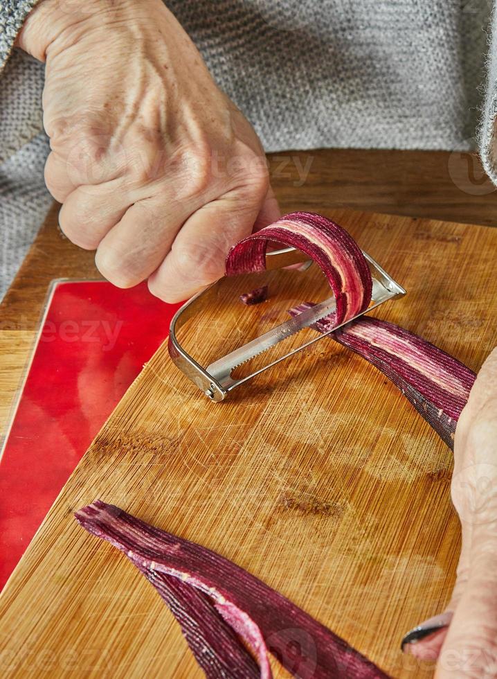 chef bezuinigingen plakjes van wortels van drie kleuren in de keuken Aan houten bord foto