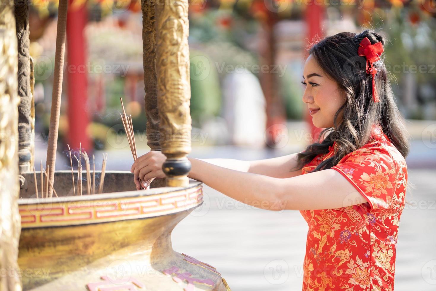 gelukkig Chinese nieuw jaar. Aziatisch vrouw vervelend traditioneel cheongsam qipao jurk zetten wierook stokjes voor het beste wens zegen en mooi zo geluk in Chinese boeddhistisch tempel. foto