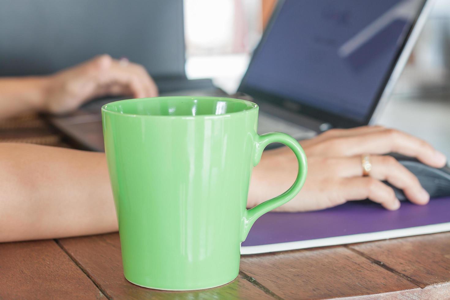 groene koffiemok met een persoon die aan laptop werkt foto