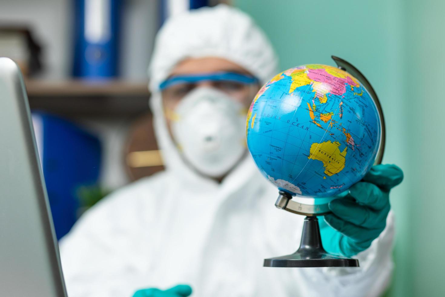 persoon in beschermend pak met earth globe met hand op kantoor foto