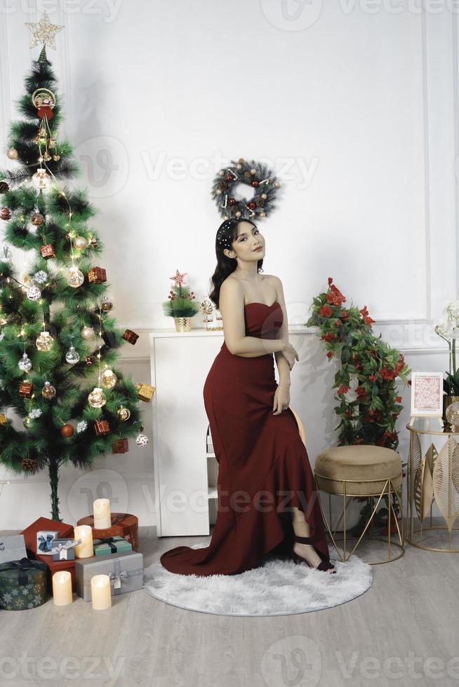 portret van een mooi jong meisje vervelend een rood gewaad, glimlachen Bij de camera, staand in versierd Kerstmis leven kamer binnenshuis foto
