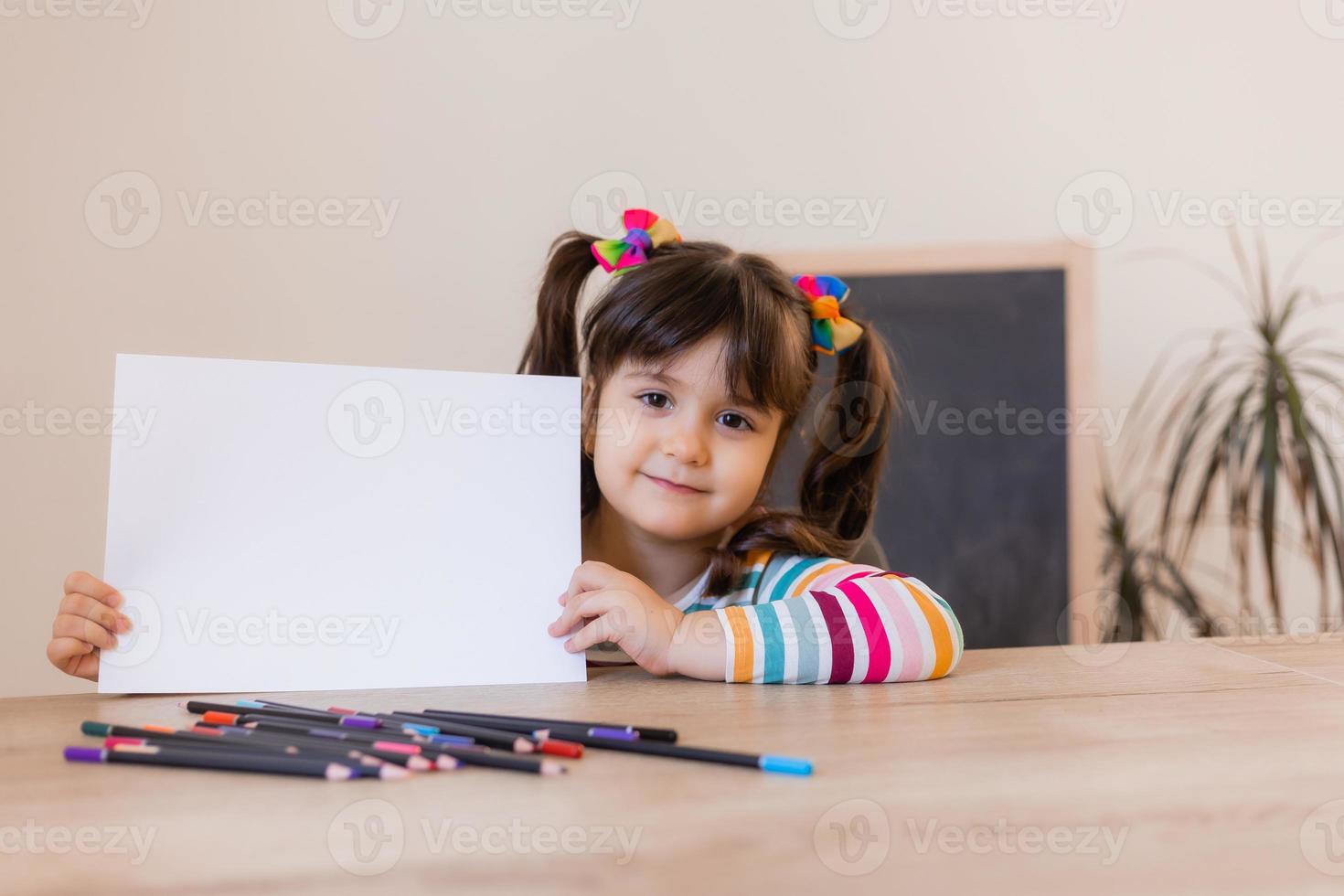 een schattig weinig meisje in een tekening les houdt een leeg wit vel in haar handen, een ruimte voor tekst. kinderen en creativiteit. hoog kwaliteit foto