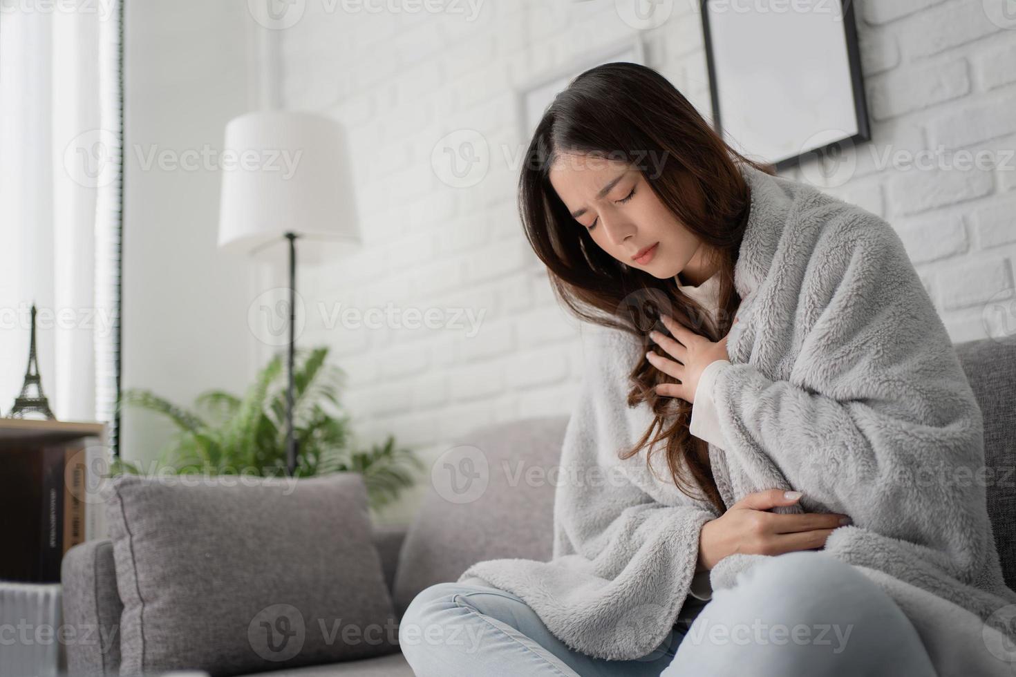 mooi Aziatisch vrouw ziek met pijn in borst terwijl werken Aan laptop ze was werken Aan de sofa in de leven kamer Bij huis. foto