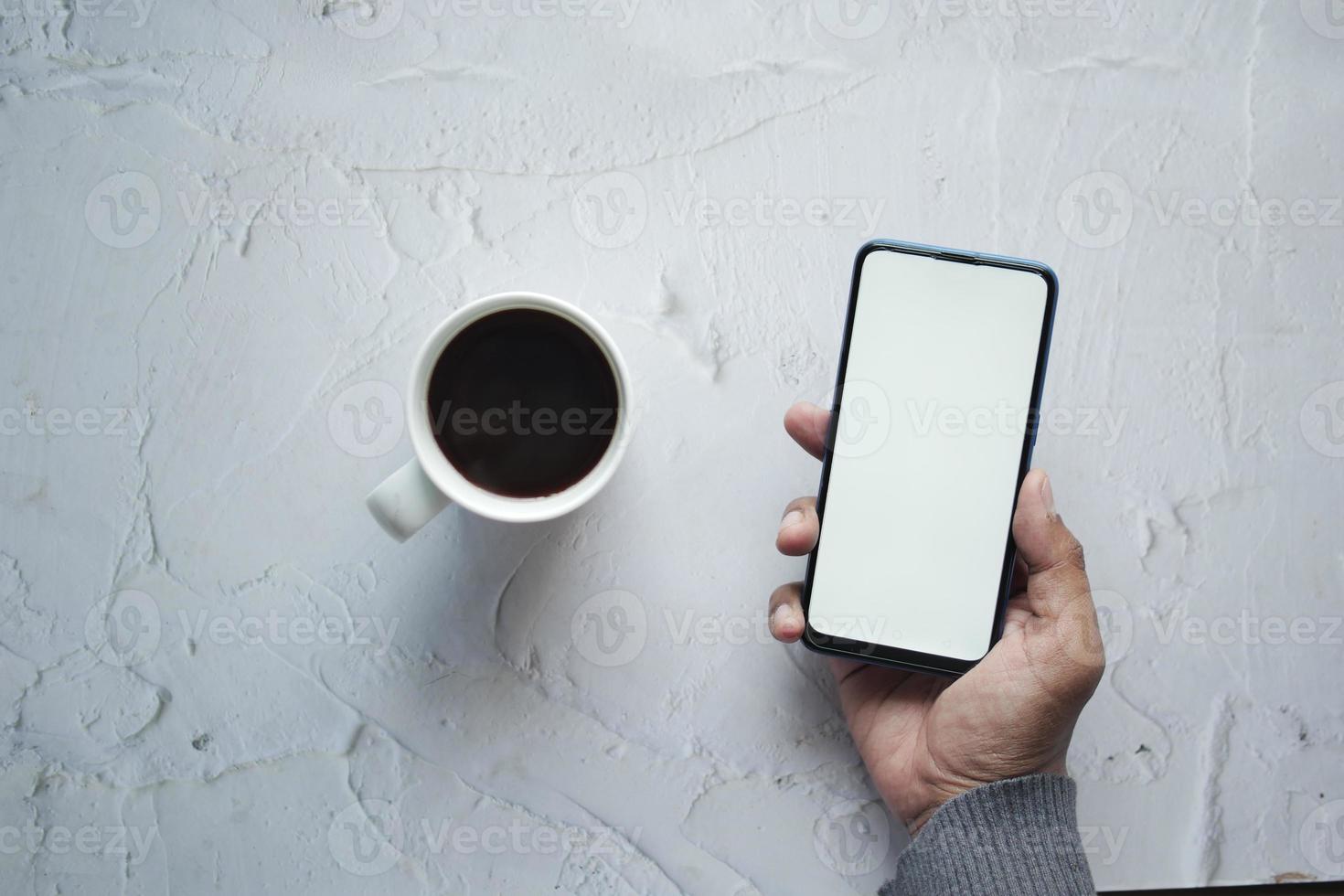 Holding een CPU van koffie en gebruik makend van slim telefoon met wit scherm foto