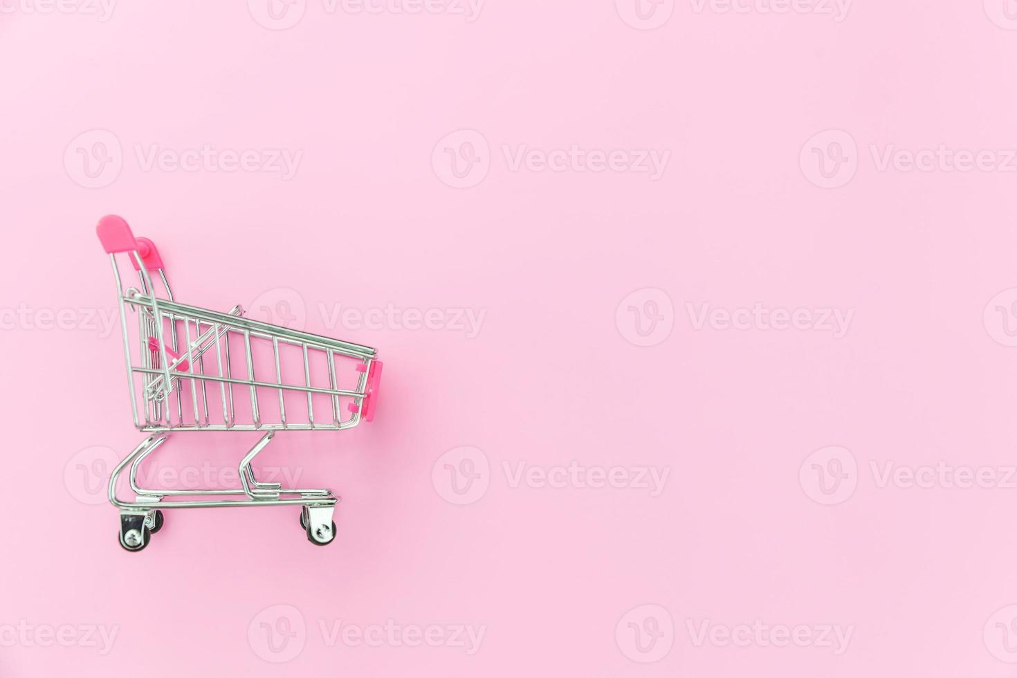 klein supermarkt kruidenier Duwen kar voor boodschappen doen speelgoed- met wielen geïsoleerd Aan roze pastel kleurrijk modieus achtergrond. uitverkoop kopen winkelcentrum markt winkel klant concept. kopiëren ruimte. foto