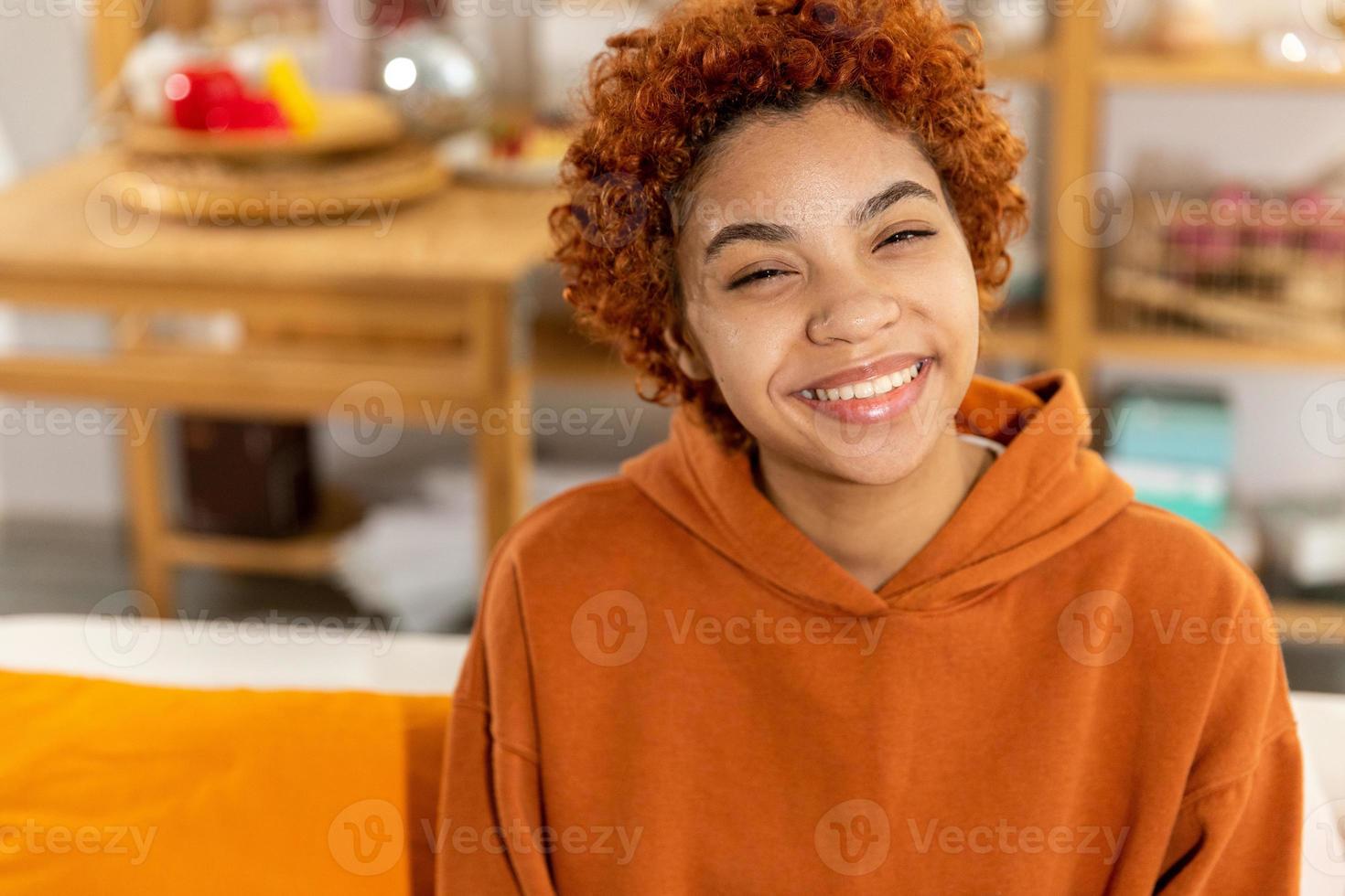mooi Afrikaanse Amerikaans meisje met afro kapsel glimlachen zittend Aan sofa Bij huis binnen. jong Afrikaanse vrouw met gekruld haar- lachend. vrijheid geluk zorgeloos gelukkig mensen concept. foto