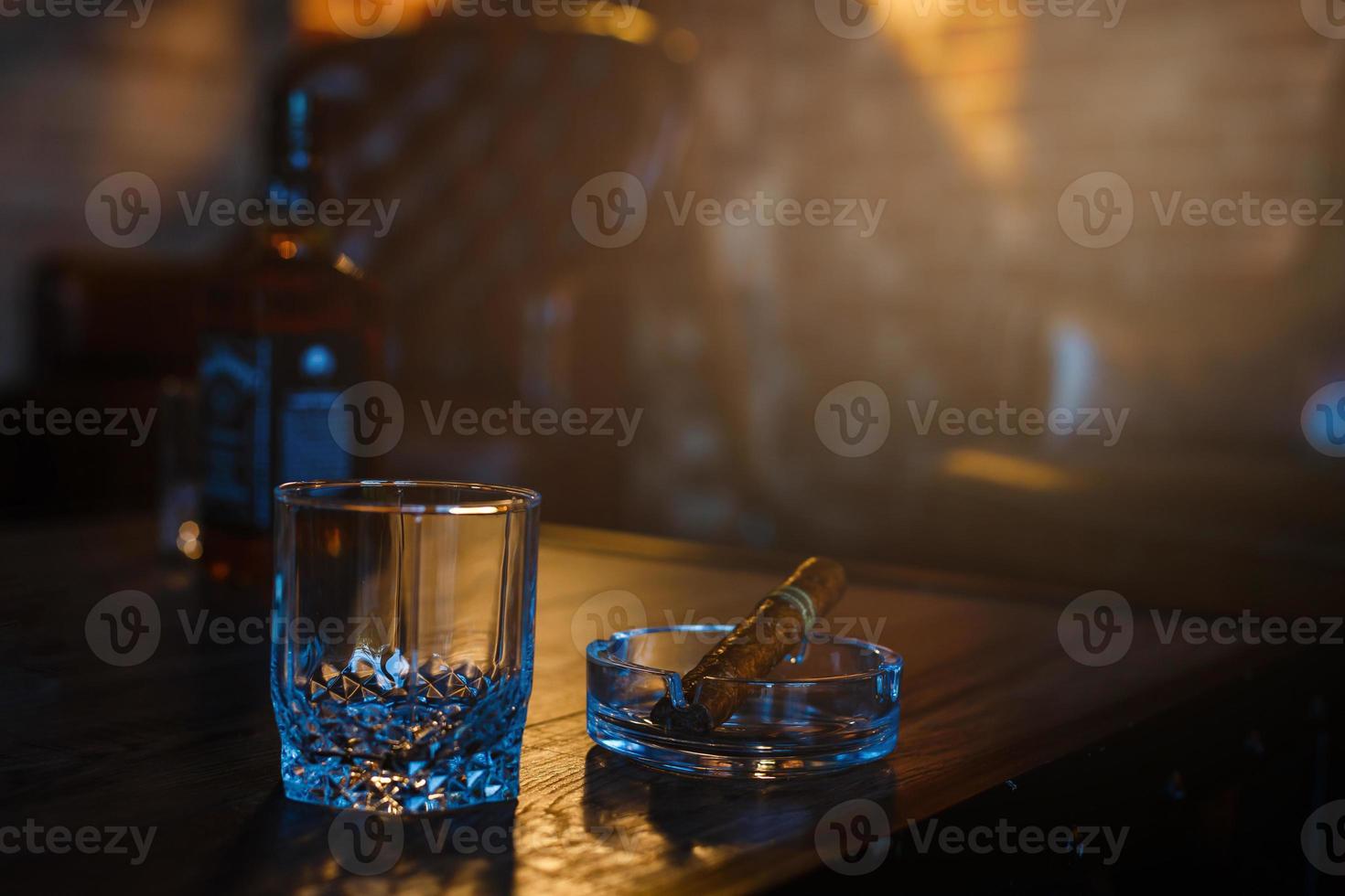 bril van whisky met roken sigaar en ijs kubussen Aan houten tafel foto