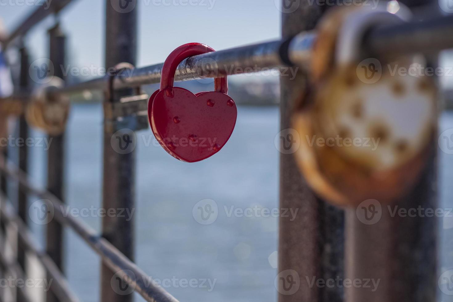 een hartvormig deur op slot doen, een symbool van liefde en trouw met een meer in de achtergrond, blijft hangen Aan de hek van de brug. de hartvormig kasteel symboliseert loyaliteit en liefde foto