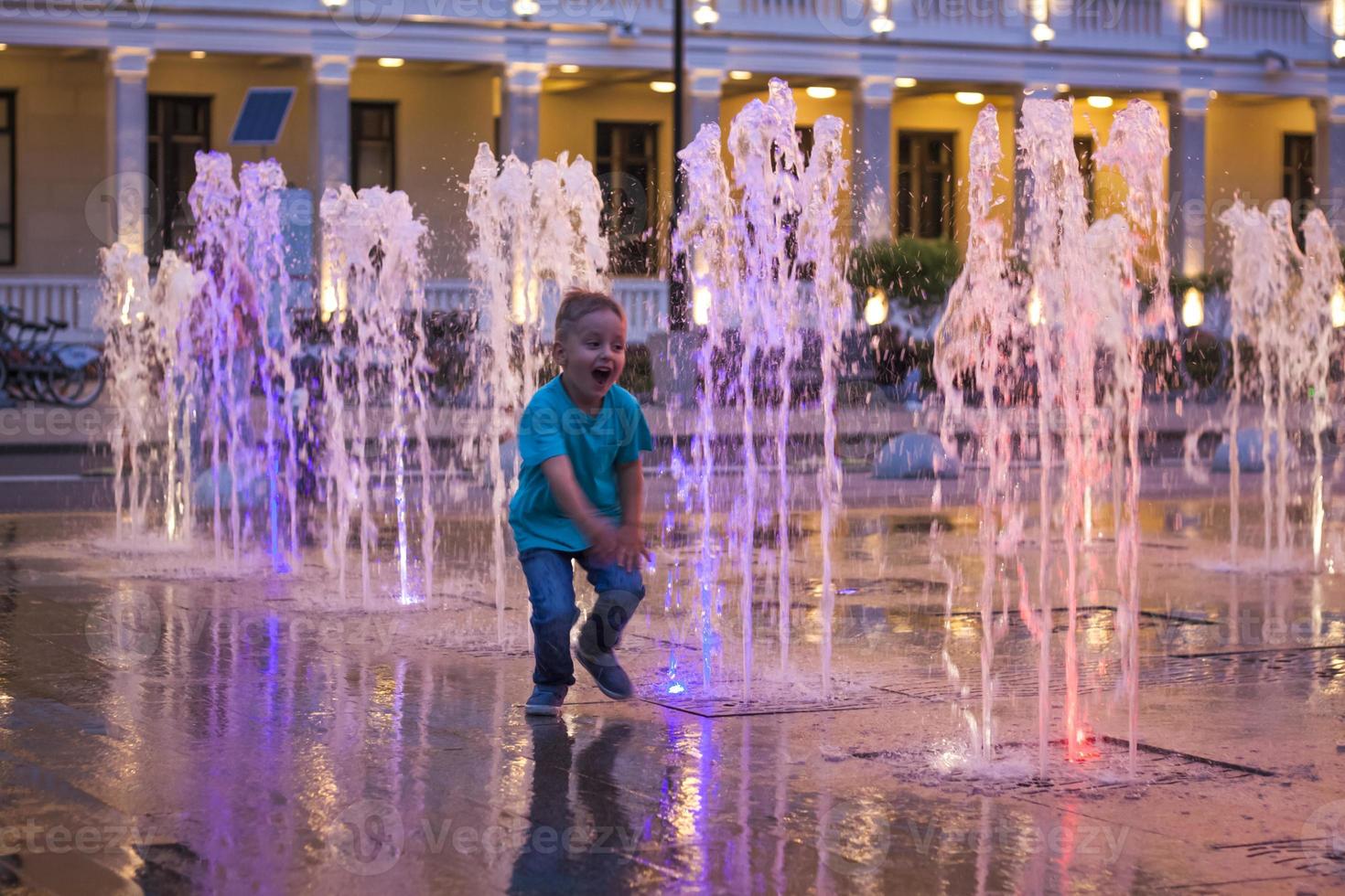 kinderen hebben pret stoeien in de fonteinen in de buurt de gebouw in de park in de zonsondergang licht. avond wandelen in de omgeving van de stad. foto