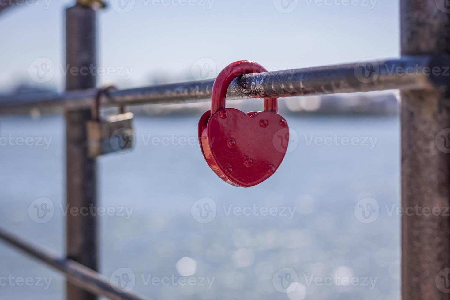 een hartvormig deur op slot doen, een symbool van liefde en trouw met een meer in de achtergrond, blijft hangen Aan de hek van de brug. de hartvormig kasteel symboliseert loyaliteit en liefde foto