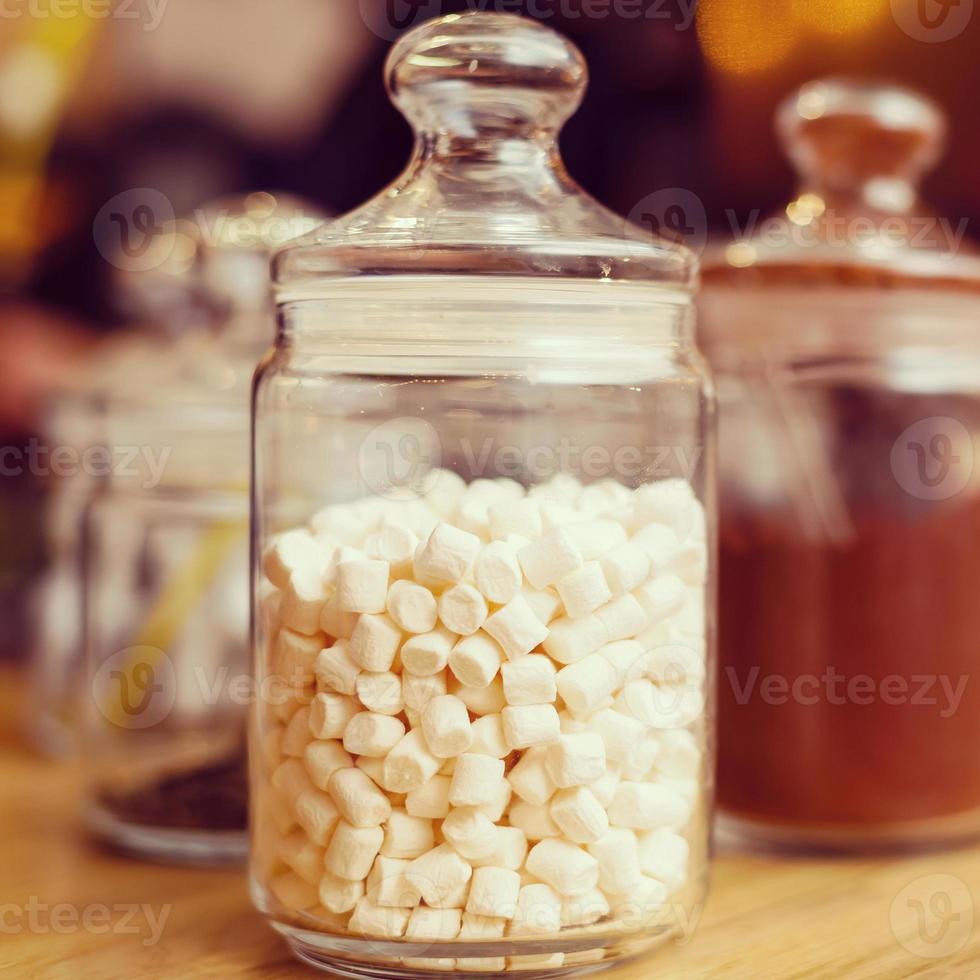 hoop van marshmallows in transparant glas pot Aan licht roze kleding achtergrond foto