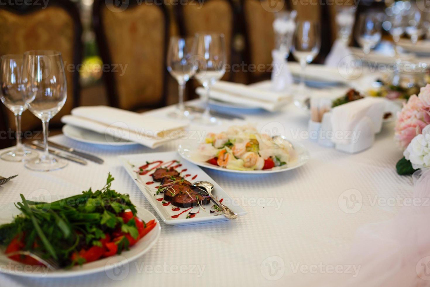 geserveerd voor een feesttafel. wijnglazen met servetten, glazen en salades. foto