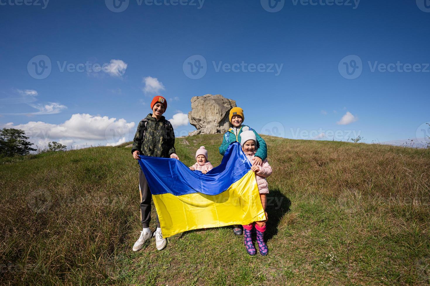 Welkom naar Oekraïne. vier kinderen houden oekraïens vlag in de buurt groot steen in heuvel pidkamin. foto