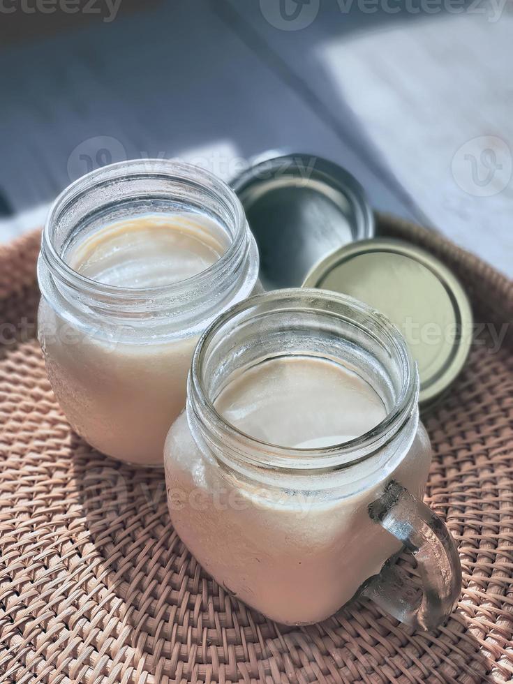 2 twee bril van metselaar potten met natuurlijk eigengemaakt duidelijk yoghurt, yoghurt, Aan de handgeweven rotan dienblad, rieten mand, hoog hoek visie. zacht thema kleur Koreaans cafe stijl, verticaal foto