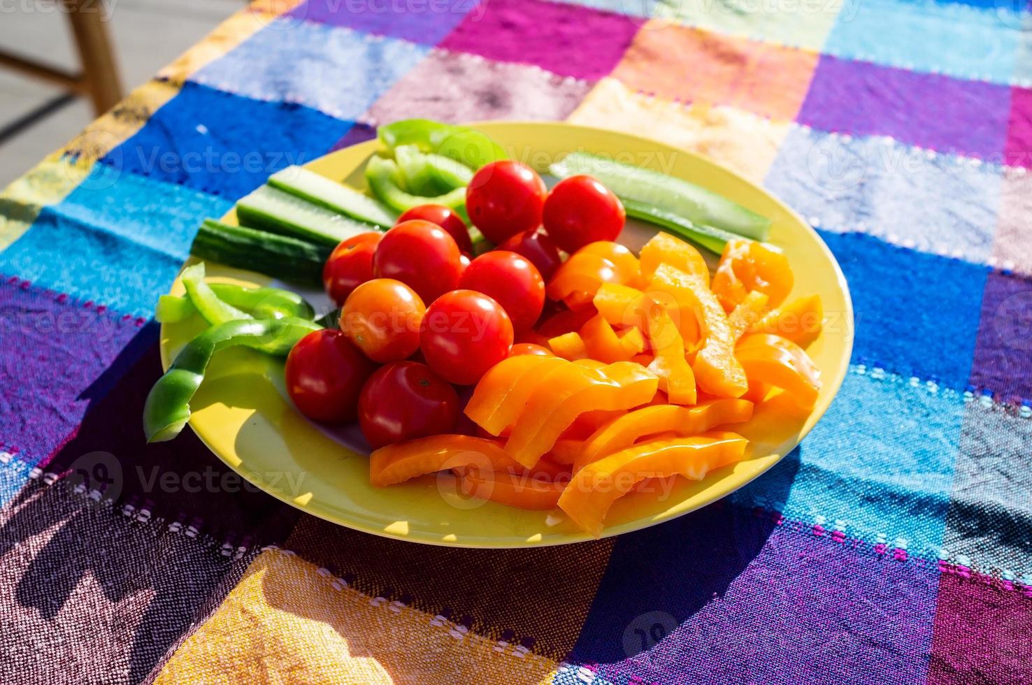 groenten Aan een bord, kers tomaten, gehakt paprika's en komkommer, Aan een tafel gedekt met een helder tafelkleed, buitenshuis. foto