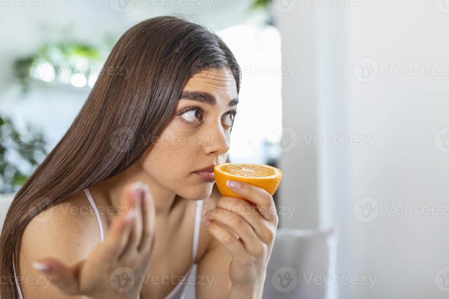 ziek vrouw proberen naar zin geur van voor de helft vers oranje, heeft symptomen van covid19, corona virus infectie - verlies van geur en smaak. een van de hoofd tekens van de ziekte. foto