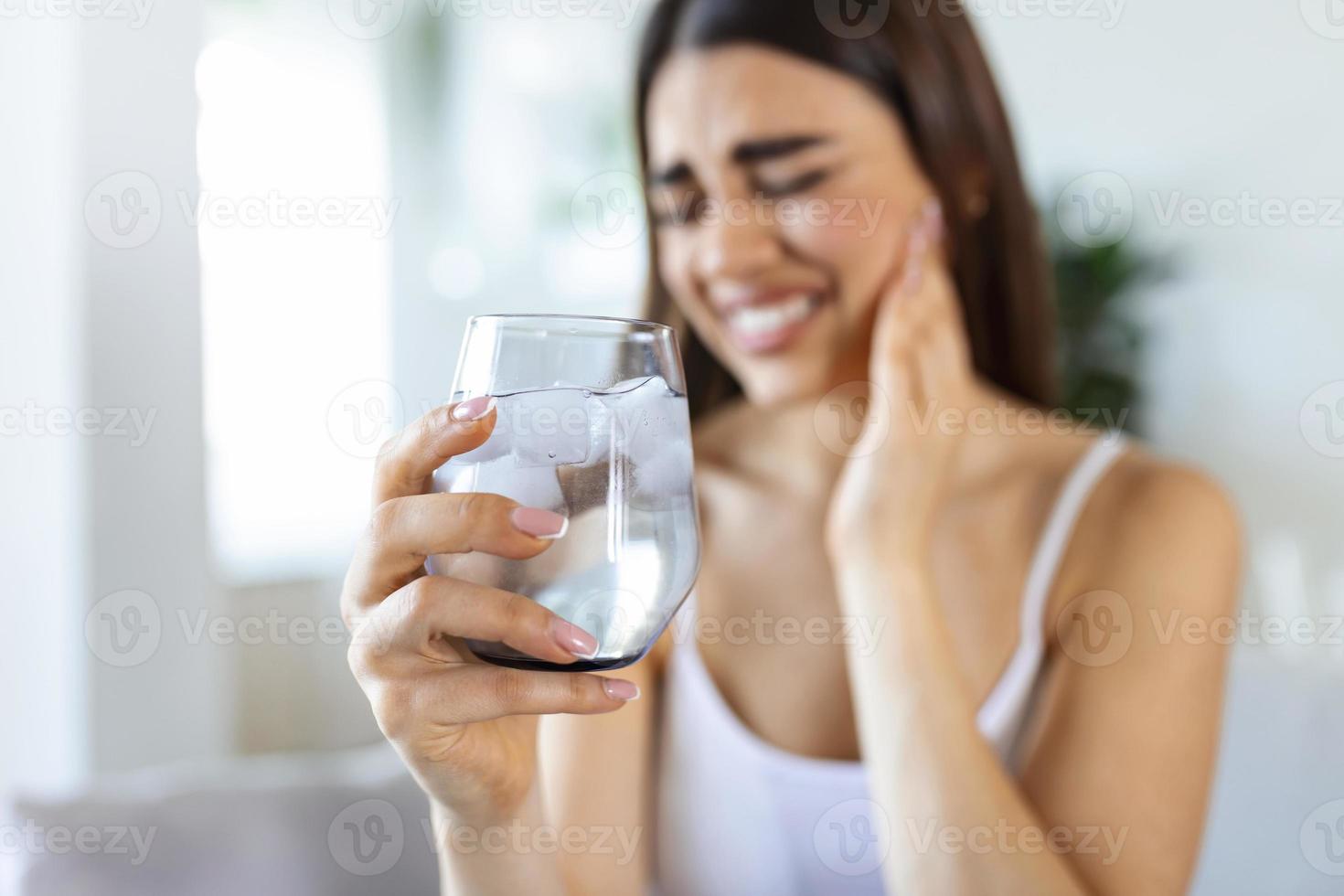 jong vrouw met gevoelig tanden en hand- Holding glas van verkoudheid water met ijs. gezondheidszorg concept. vrouw drinken verkoudheid drankje, glas vol van ijs kubussen en voelt kiespijn, pijn foto