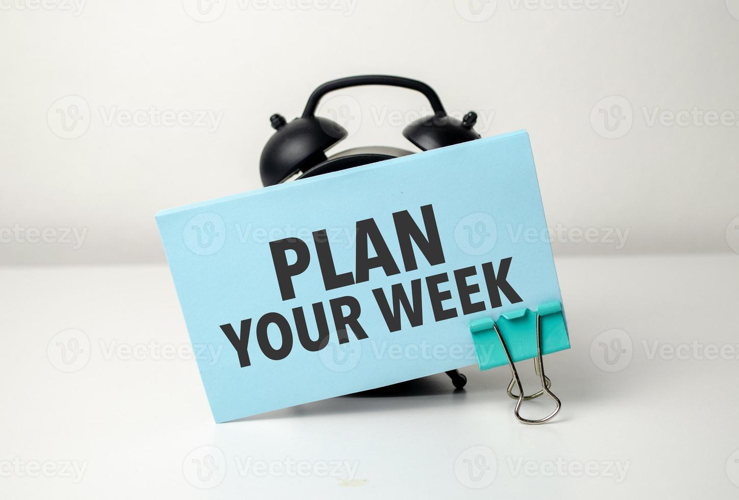 plan uw week is geschreven in een blauw sticker in de buurt een zwart alarm klok foto