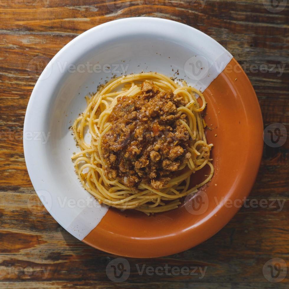 gezond bord van Italiaans spaghetti bekroond met een smakelijk tomaat en grond rundvlees bolognese saus en vers basilicum Aan een rustiek bruin houten tafel foto